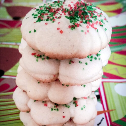 A stack of cookie press almond spritz butter cookies coated in red and green sugar sprinkles for the holidays