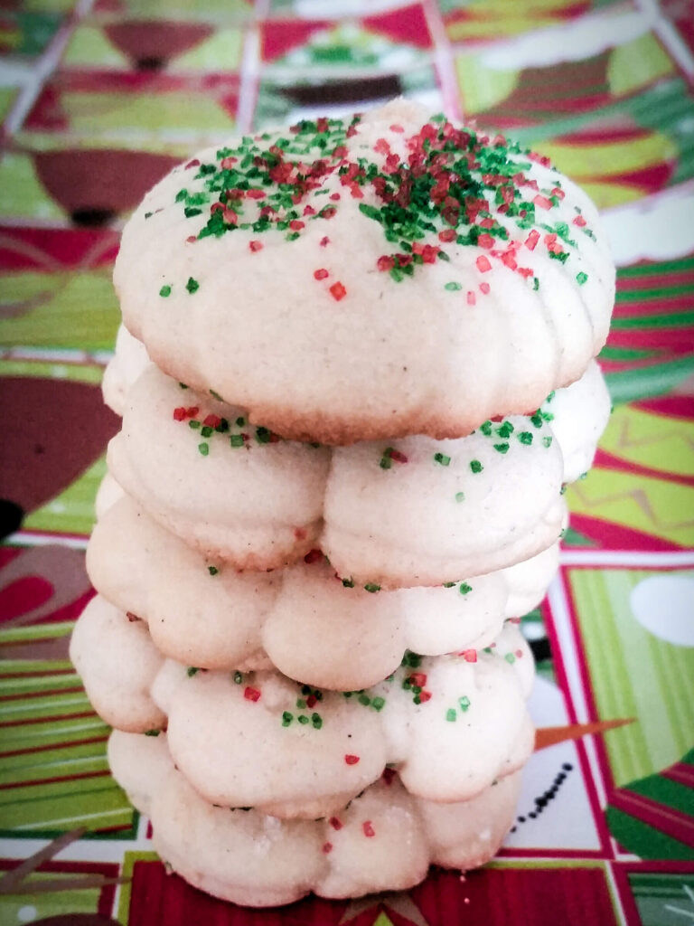 A stack of cookie press buttery almond spritz cookies coated in red and green sugar sprinkles for the holidays
