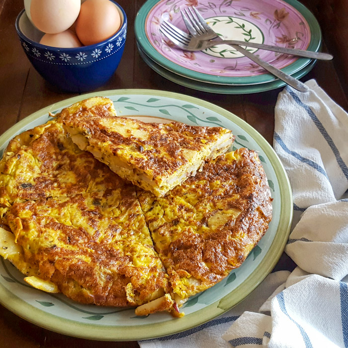 Authentic Spanish tortilla española sliced into wedges on pale green patterned plate showing creamy egg and potato layers