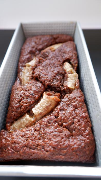 Chocolate zucchini banana bread batter in a loaf pan topped with a halved banana and sprinkled with raw sugar before baking