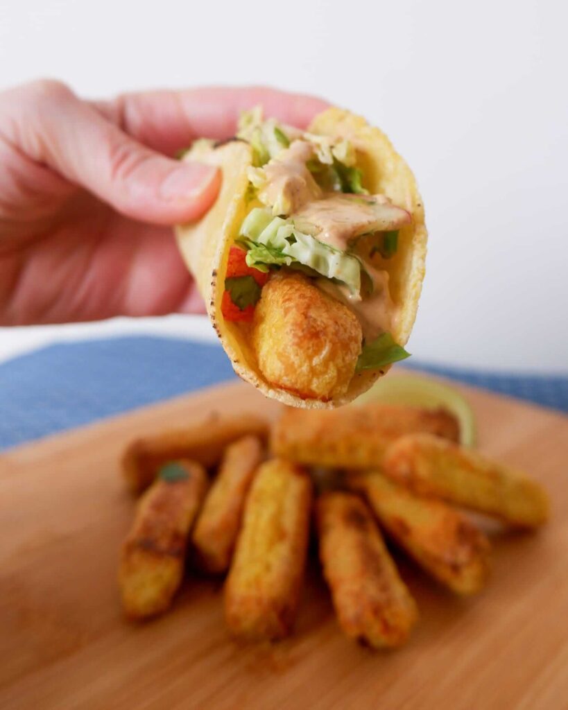 Close-up of assembled fish stick tacos on corn tortillas, topped with vibrant fennel apple slaw, drizzled sriracha aioli, and lime wedges—crispy, fresh weeknight perfection.