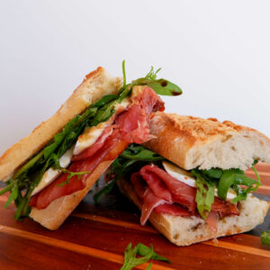 Presunto, fig, and brie sandwich on rustic wood board with arugula and honey drizzle