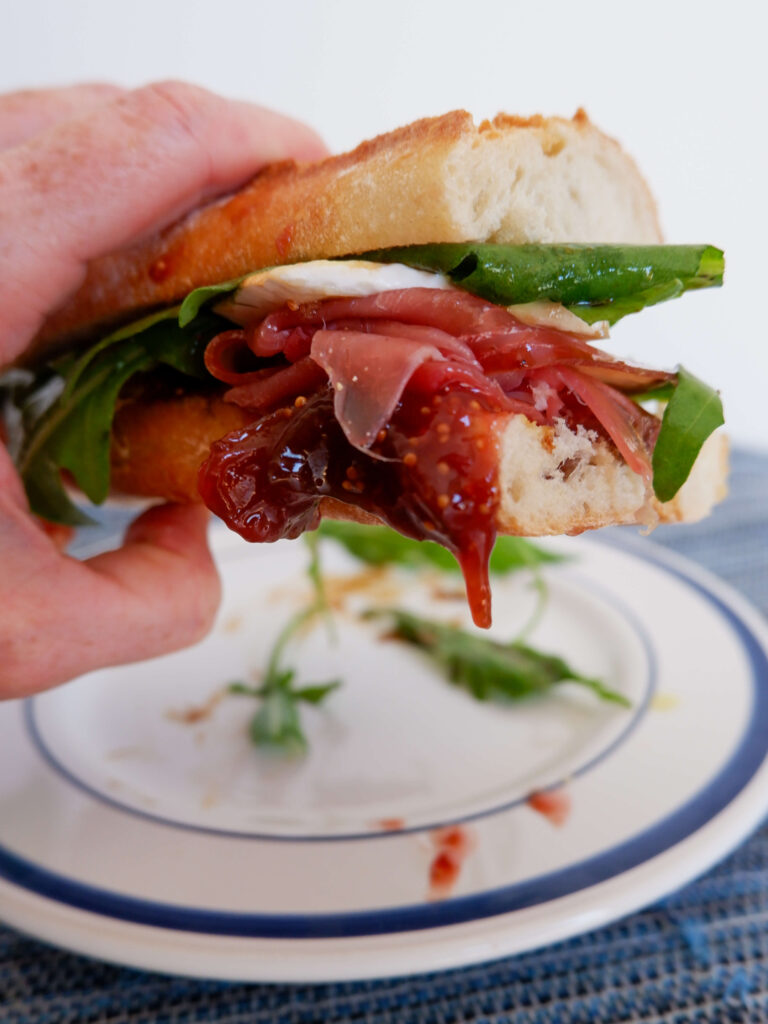 Close-up of fig jam and sliced brie layered on baguette with Portuguese presunto