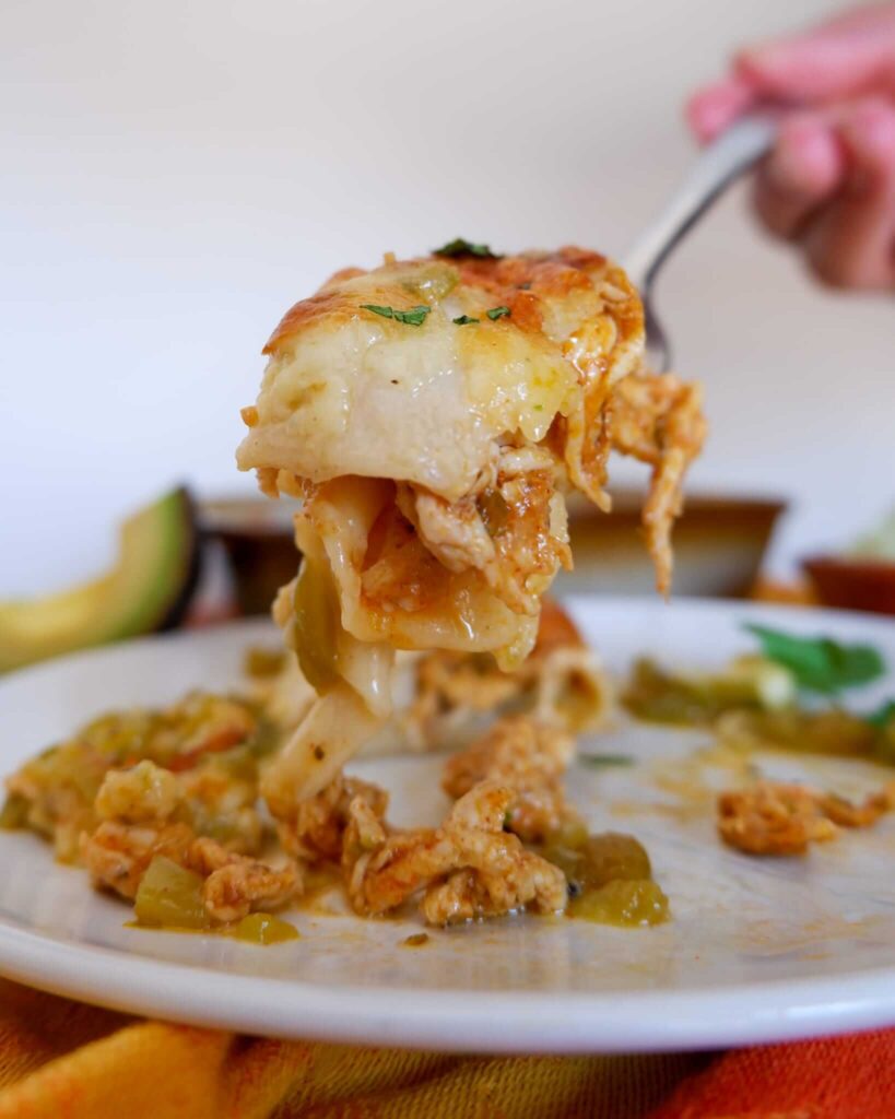 Green chile chicken enchiladas in a baking dish topped with melted white cheese and crispy tortilla edges