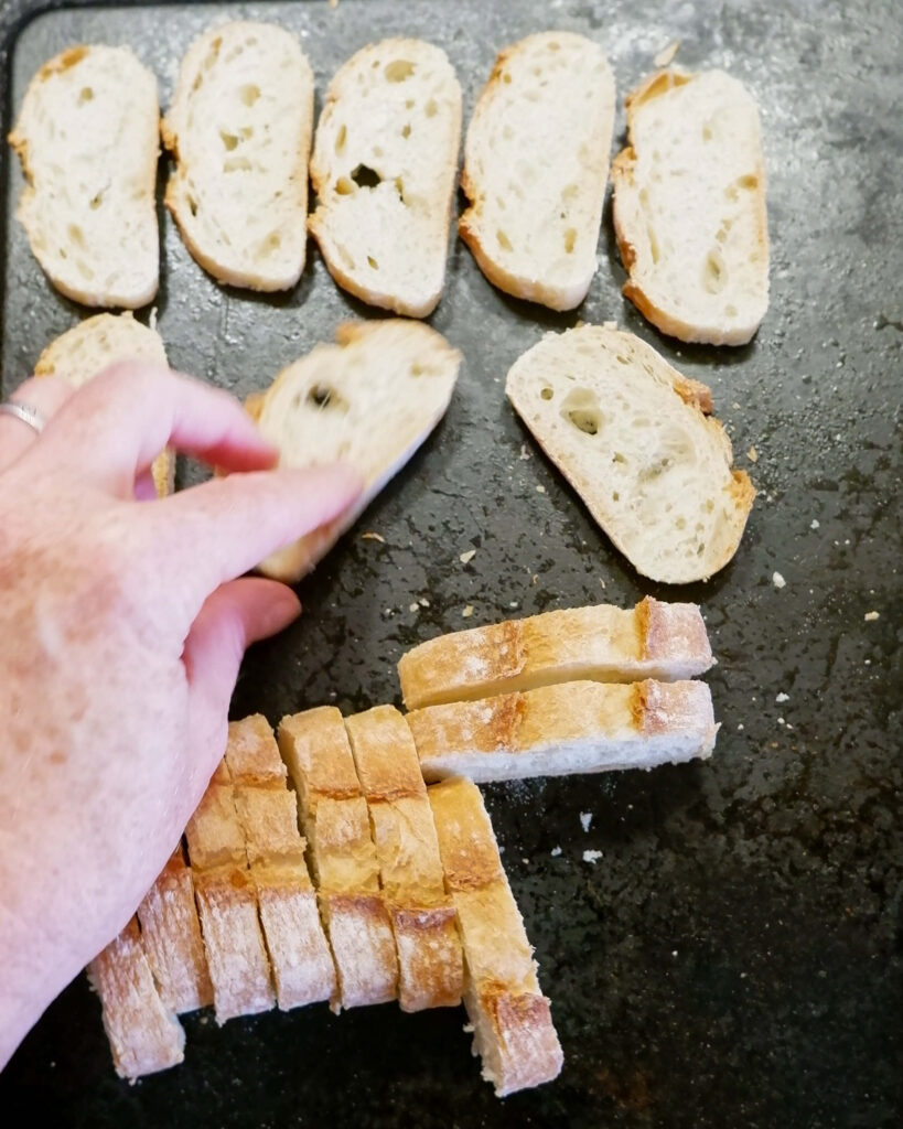 Broiled baguette slices on parchment-lined baking sheet, golden and ready for toppings