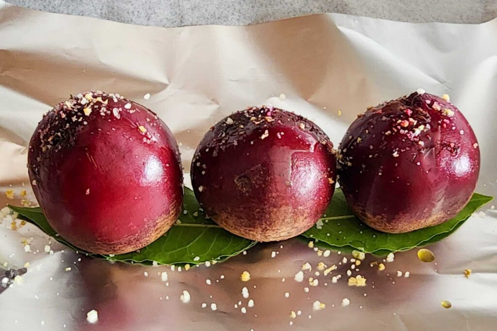 Whole red beets sitting on fresh bay leaves on double-layered foil, ready to roast