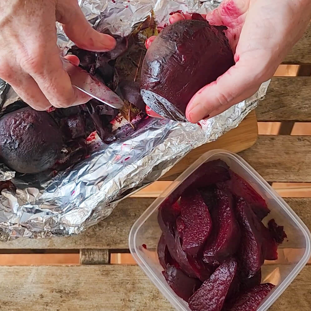 Butter knife sliding the skin off a warm roasted beet with a bowl of cut beet wedges