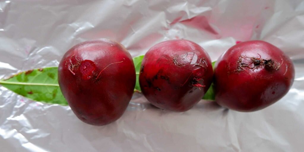Whole unpeeled beets with tops trimmed flat, sitting on fresh bay leaves on double-layered foil