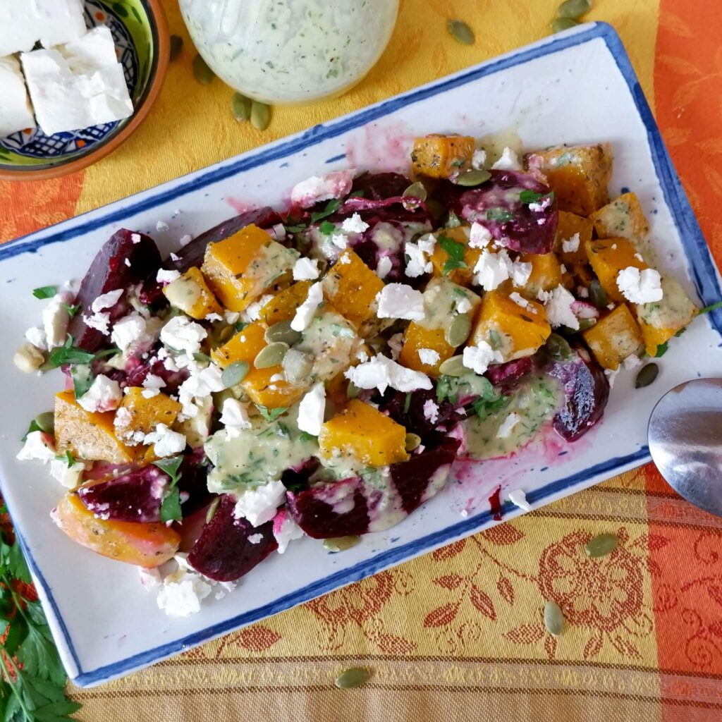 Roasted beet salad with golden butternut squash cubes, crumbled feta, parsley, and pumpkin seeds in a serving dish